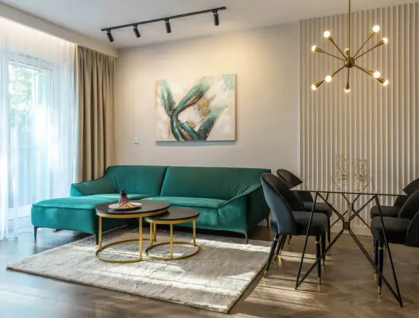 Butelkowa zieleń sofy i dodatki do salonu tworzą elegancką przestrzeń. Szare krzesła i szklany stół dodają nowoczesności.
