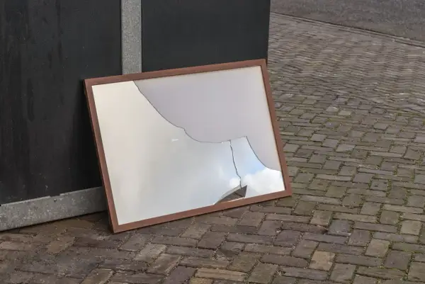 Zepsute lustro w drewnianej ramie leży na bruku. Czy lustro można wyrzucić do szkła?
