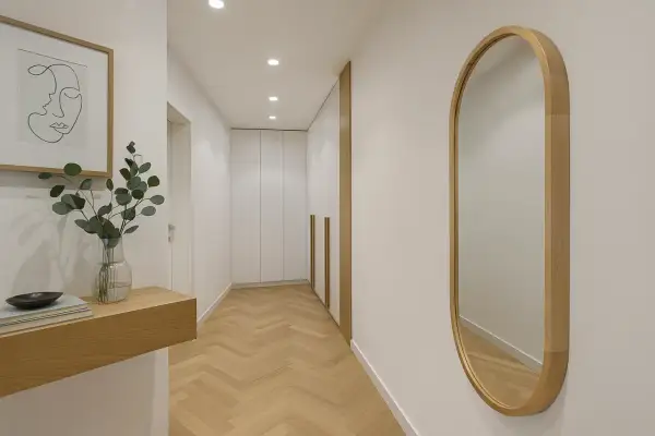 Eleganckie lustro owalne w drewnianej ramie odbija światło w nowoczesnym korytarzu z parkietem w jodełkę.