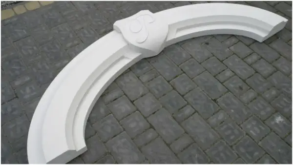 Biały, ozdobny łuk nad drzwiami z herbem, gotowy do montażu. Idealny, by nadać wejściu elegancki charakter.