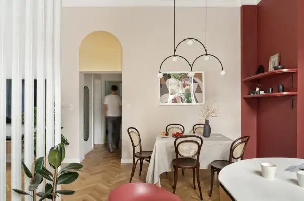 Złote łuki na ścianie dodają elegancji wnętrzu. W jadalni stół nakryty obrusem, krzesła z rattanu, a nad nimi nowoczesna lampa.