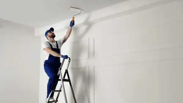 Malarz na drabinie odświeża sufit. Zastanawiasz się, co ile lat malować sufit? To zależy od materiału i warunków.