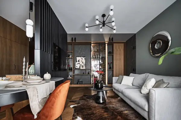 Eleganckie aranżacje nowoczesny salon: szara sofa, pomarańczowy fotel, drewniana podłoga i designerskie oświetlenie tworzą przytulną przestrzeń.