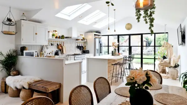 Jasna kuchnia w stylu modern farmhouse z wyspą, białymi meblami i drewnianymi akcentami. Dachowe okna wpuszczają mnóstwo światła.