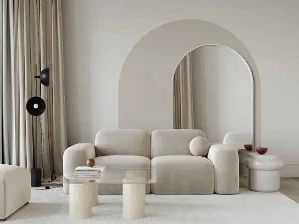 Nowoczesny salon z łukiem w tle. Beżowa kanapa, szklany stolik i lustro w łukowatej ramie tworzą stylowe inspiracje.