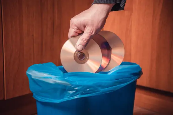 Dłoń wrzuca płyty CD do niebieskiego kosza. Zastanawiasz się, gdzie wyrzucić płyty GK?
